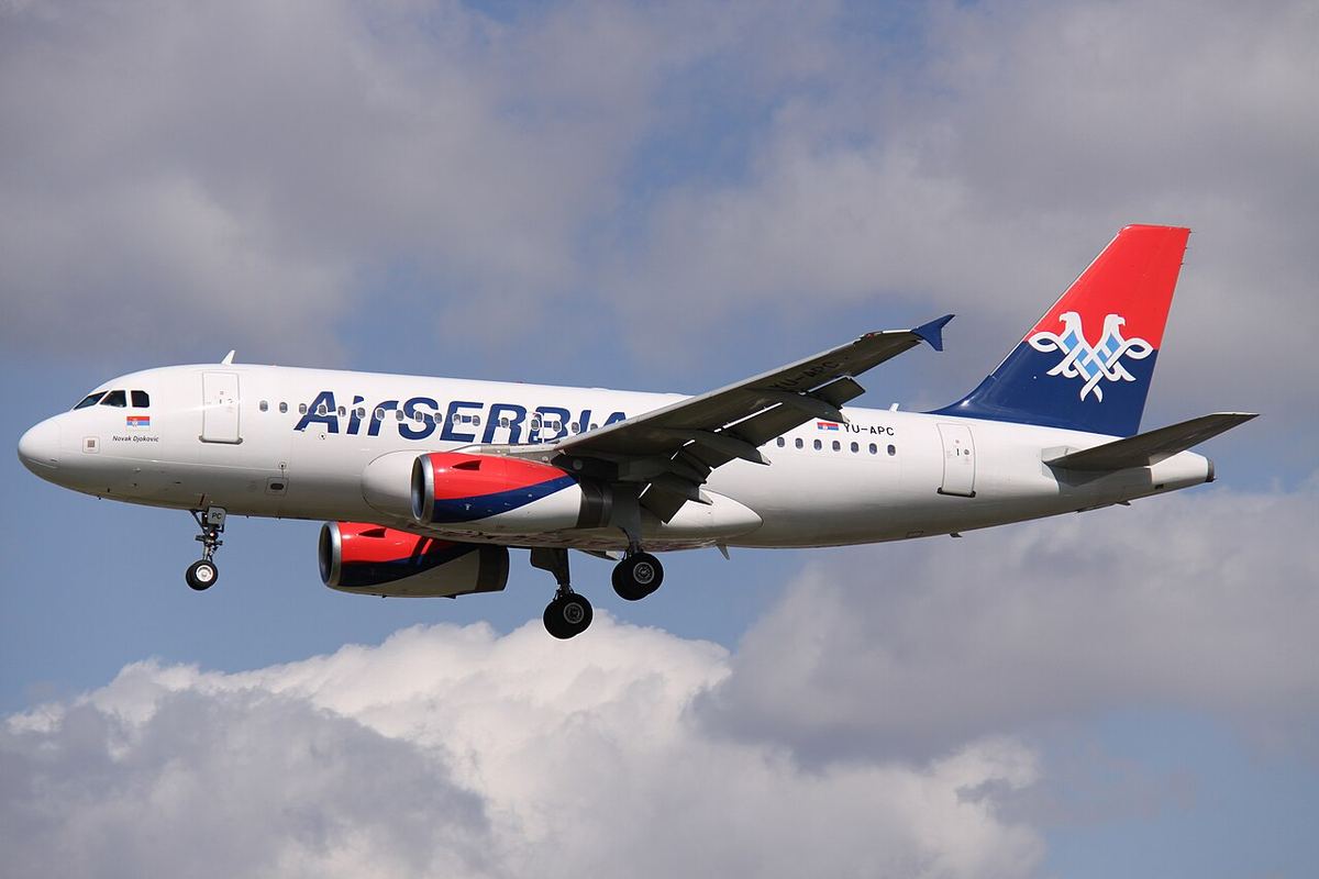 Avion Air Serbia Airbus A319 în zbor, cu livrea albă, roșie și albastră, pe fundal de nori.