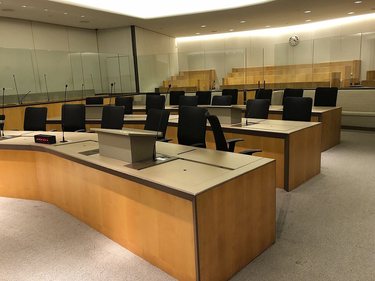 Sală de judecată goală, cu mese de lemn, scaune negre, microfoane și paravane de sticlă. Imagine ilustrativă.