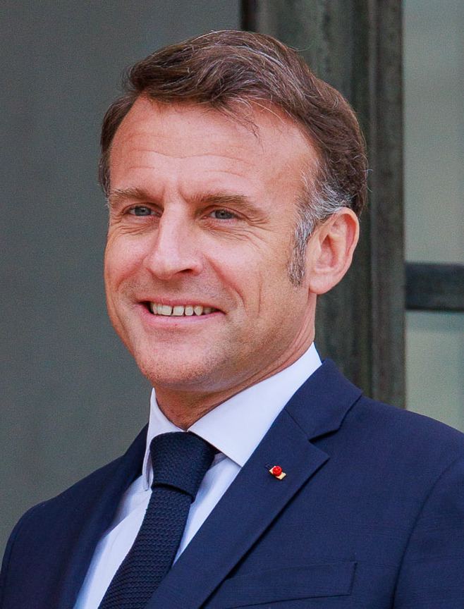 Emmanuel Macron, președintele Franței, zâmbind, în costum bleumarin și cămașă albă (fotografie de arhivă).