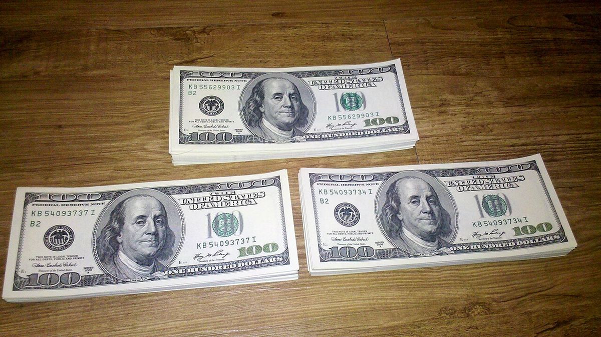 Teancuri de bancnote americane de 100 de dolari așezate pe o suprafață de lemn.