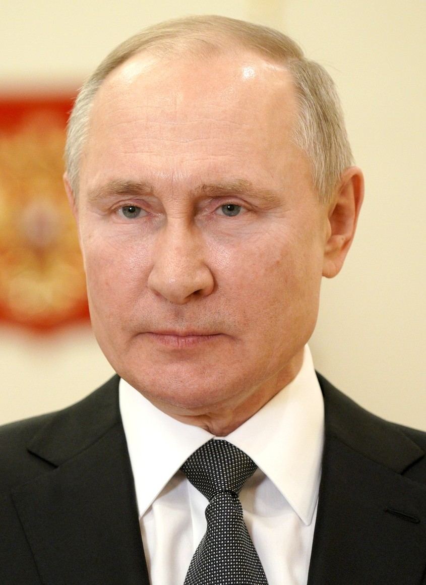 Portretul fostului președinte Vladimir Putin, în costum închis și cravată, în fața unui fundal cu emblemă roșie (fotografie de arhivă).