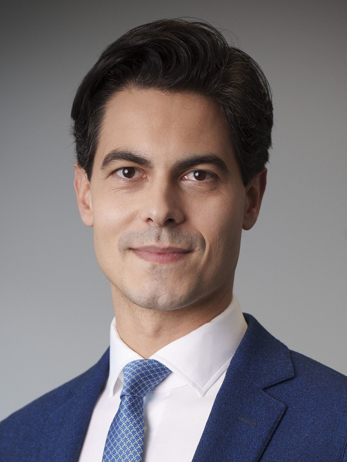 Portretul premierului olandez Rob Jetten, într-un costum albastru și cămașă albă, cu cravată albastră, pe fundal gri.