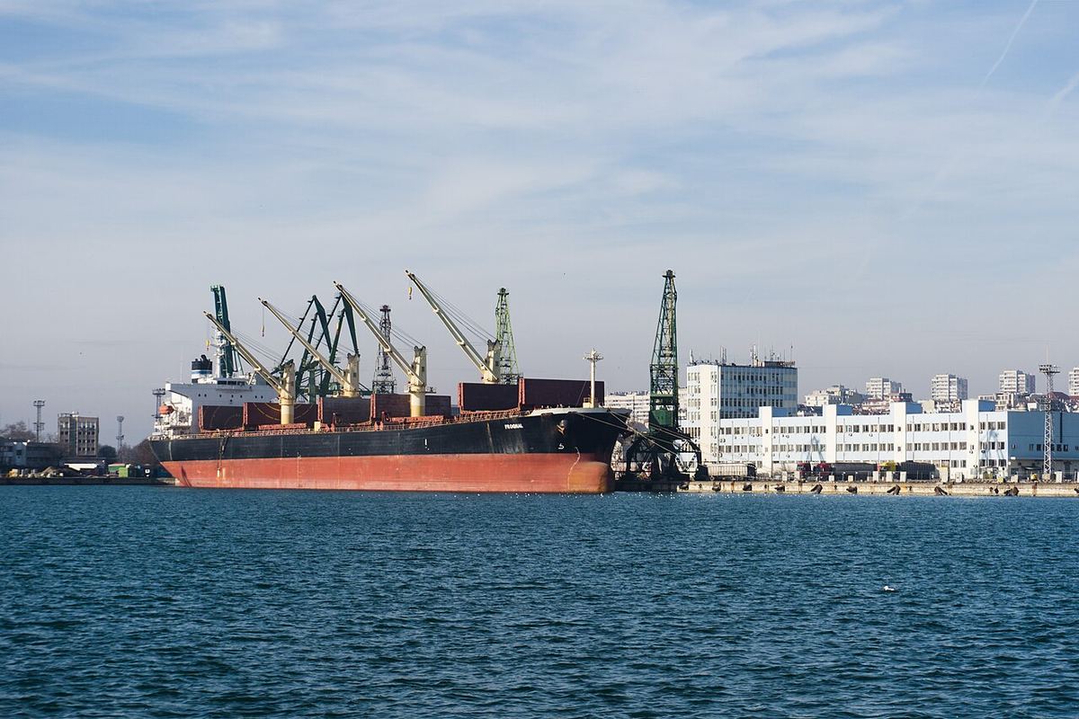 Navă de marfă cu corp roșu, andocată în portul Varna, lângă macarale și containere (fotografie de arhivă).