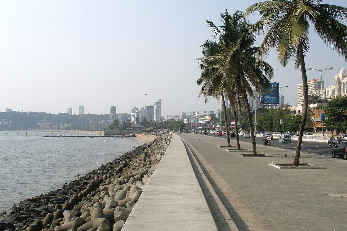 Promenada Back Bay din Mumbai, cu palmieri, blocuri de beton pe mal și clădiri înalte în fundal, pe timp de zi.