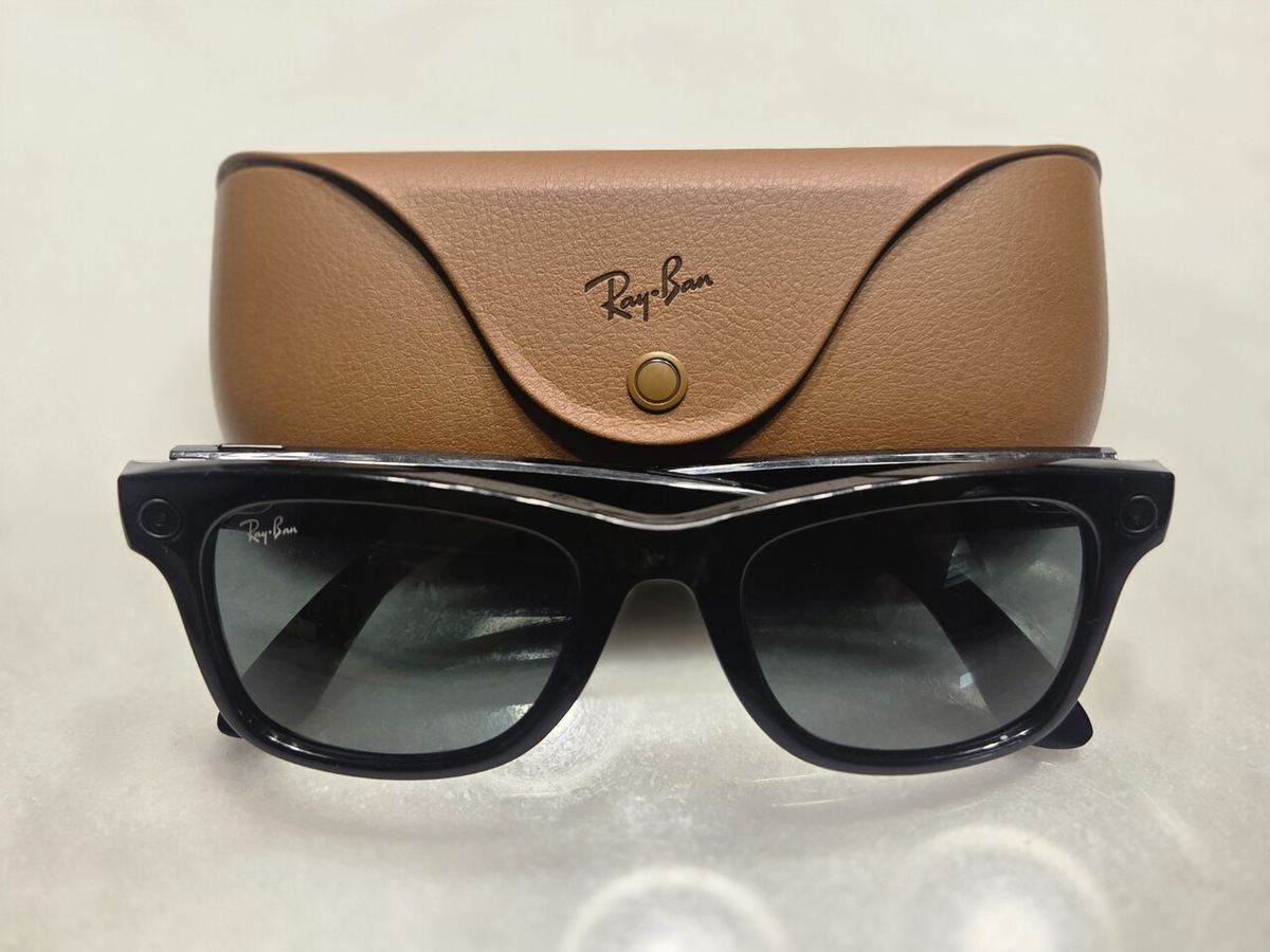 Ochelari inteligenți Ray-Ban Meta negri, lângă carcasa maro din piele de încărcare.