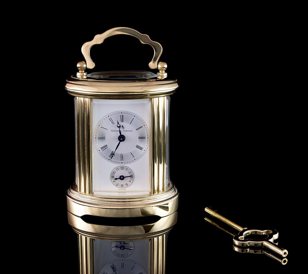 Ceas de călătorie (carriage clock) de la Matthew Norman, cu cheia de întors arcul, de aproximativ 10 cm înălțime.