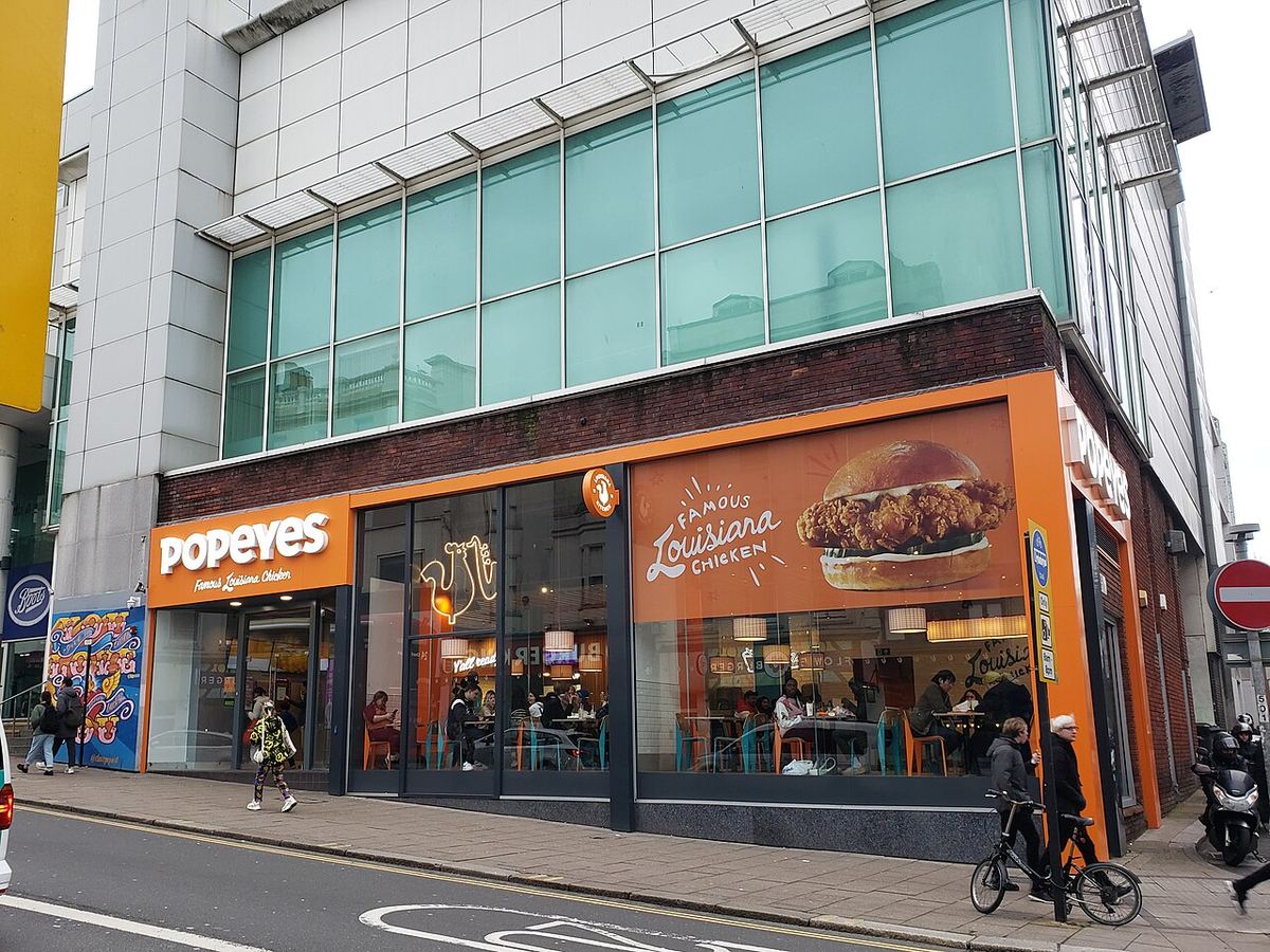 Vitrina unui restaurant Popeyes cu logo portocaliu și clienți în interior, în Brighton, Marea Britanie (fotografie de arhivă)