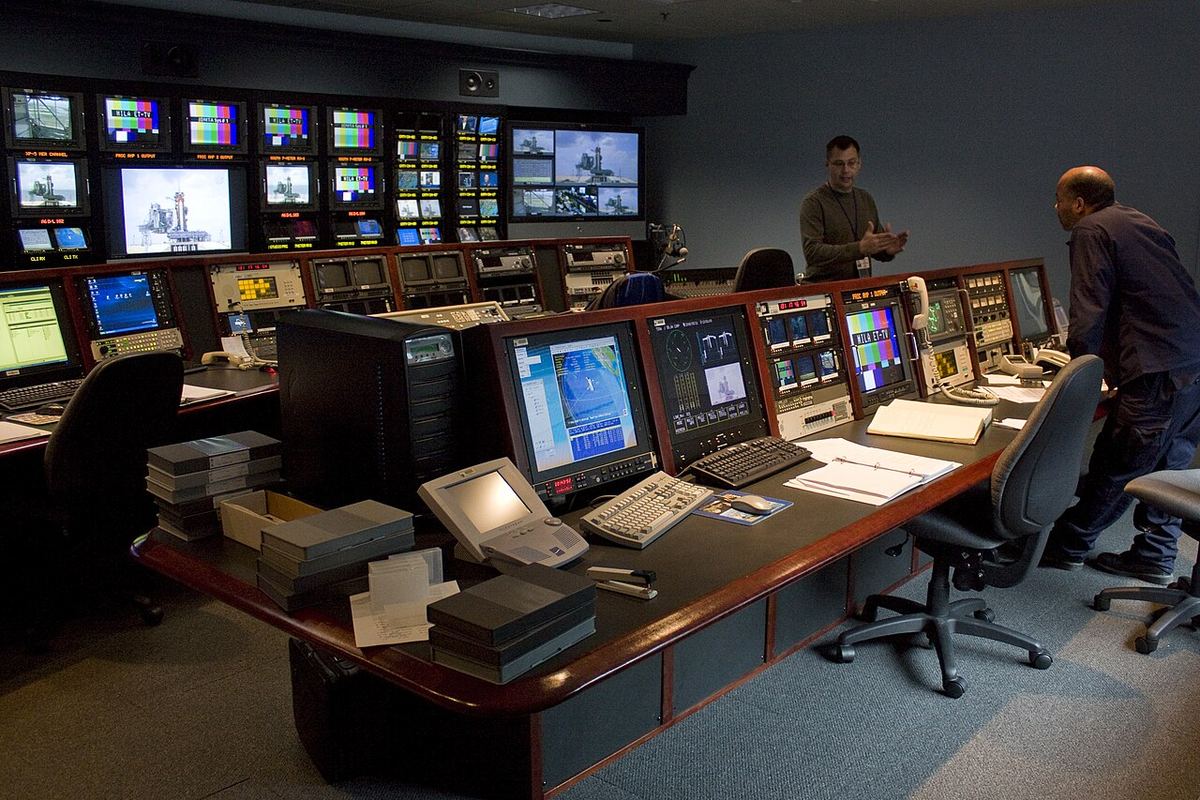 Doi tehnicieni de televiziune discută într-o sală de control la centrul Goddard al NASA, în fața unor monitoare.