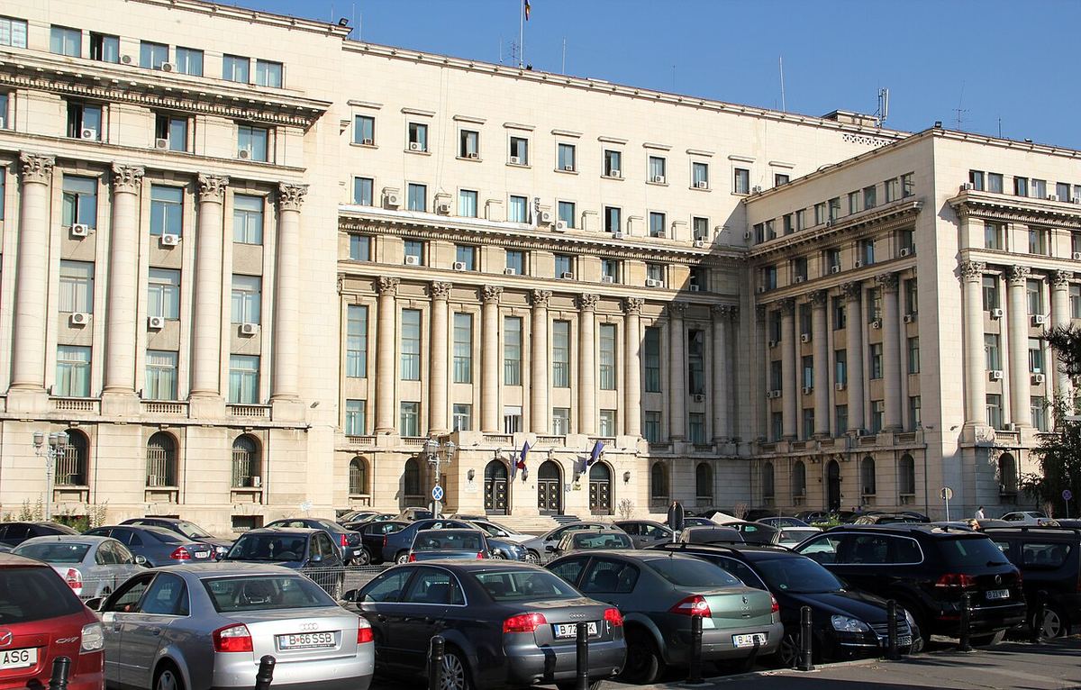 Fațada unei clădiri administrative masive din perioada comunistă, cu balcon central, fotografiată din exterior.
