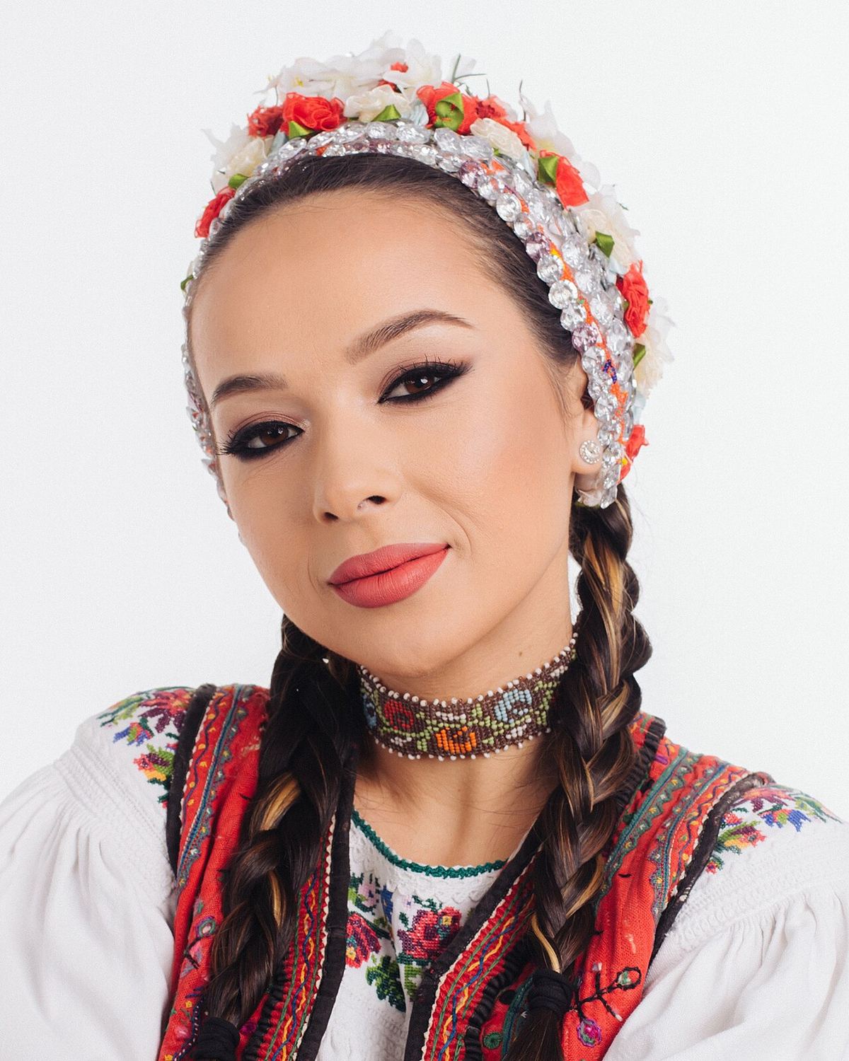 Portretul cântăreței Vlăduța Lupău, în costum popular tradițional cu cunună de flori și salbă, pe fundal alb.