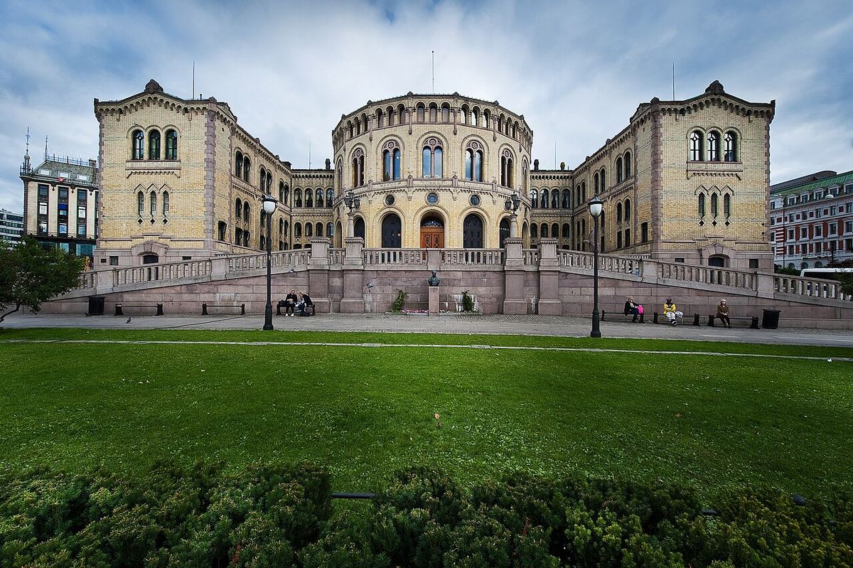 Clădirea Stortingului (parlamentul Norvegiei) din Oslo, fotografiată din fața unui parc cu gazon verde.