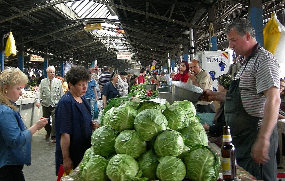 Cumpărători și comercianți la Piața Obor din București, printre grămezi mari de varză proaspătă.