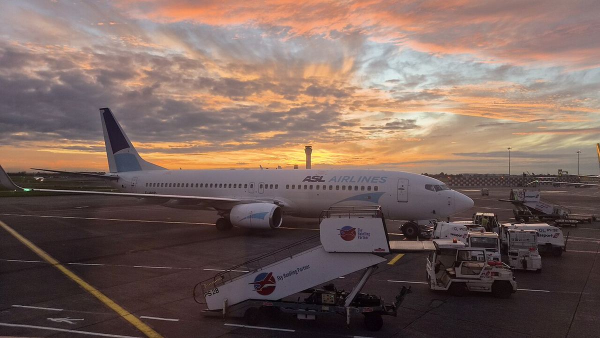 Avion de pasageri pe platforma unui aeroport din Dublin, la apus, cu vehicule de servire la sol.