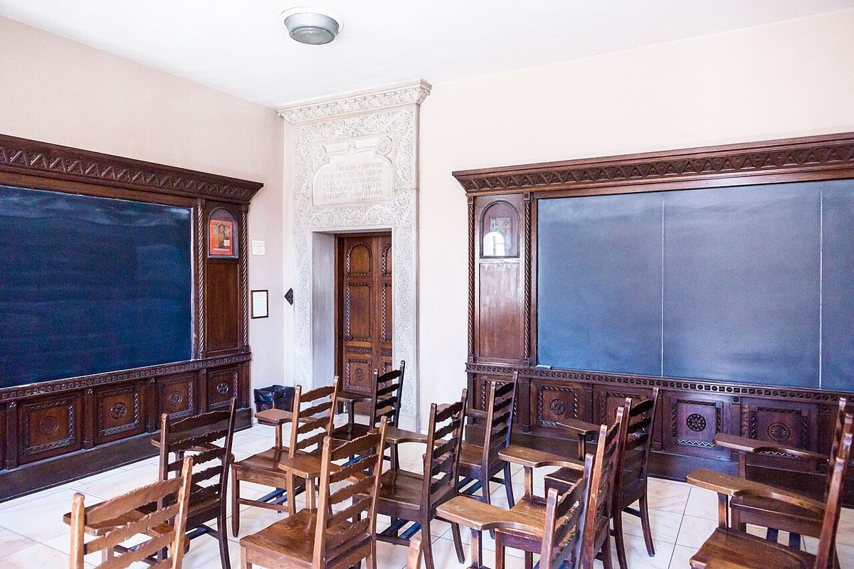 Sală de clasă goală, cu tablă și scaune de lemn