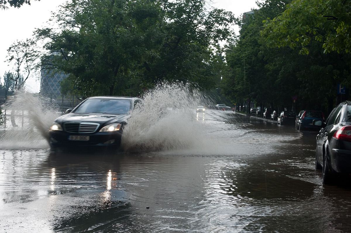 Mașină care trece printr-o băltoacă mare pe un bulevard, după o ploaie torențială