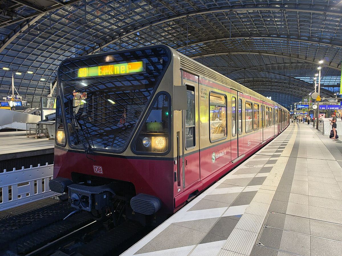 Tren S-Bahn roșu-bordo în peronul Gării Centrale Berlin, Germania, cu afișaj pe frontal și pasageri în fundal.