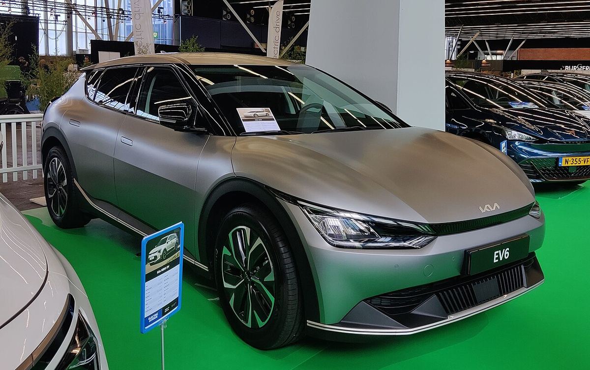 Kia EV6 electric, de culoare gri mat, fotografiat din față la un salon auto din Amsterdam.
