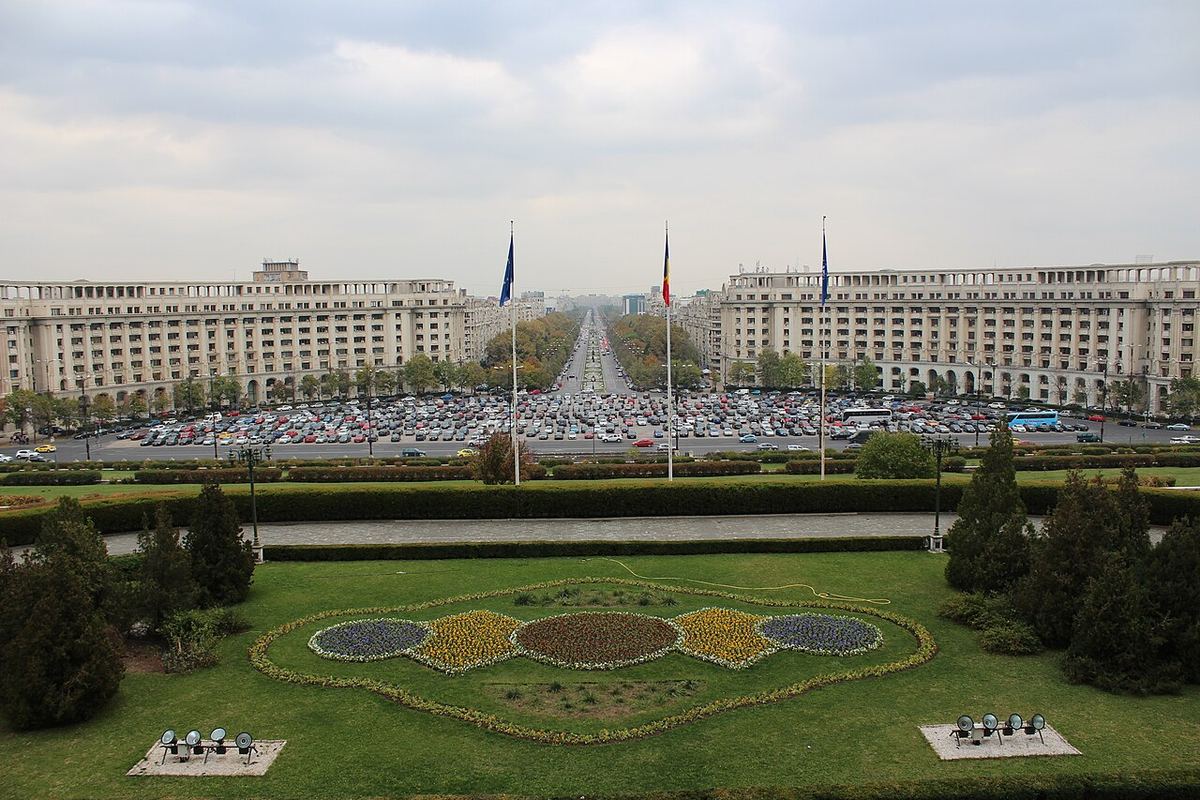 Palatul Parlamentului din București, vedere aeriană cu drapele, parcare și grădini în prim-plan.