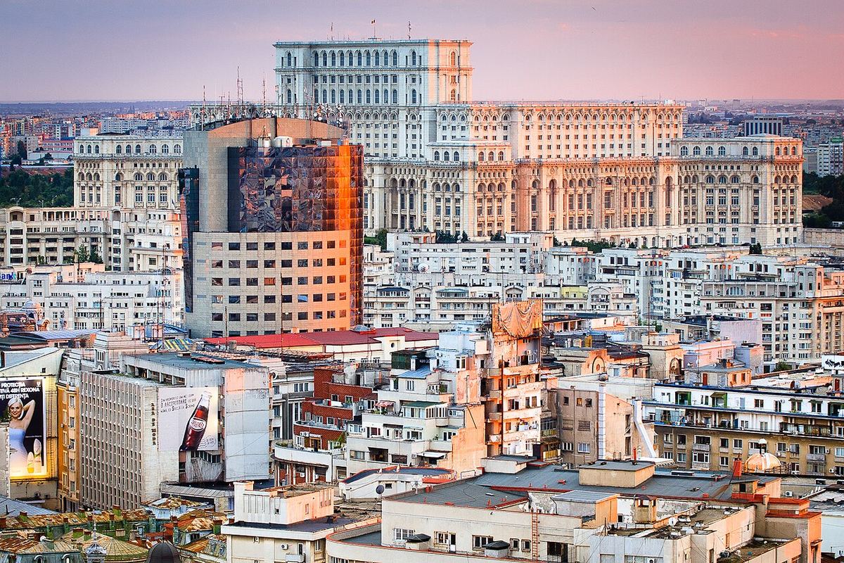 Palatul Parlamentului din București, fotografiat din înălțime, cu blocuri de locuințe și clădiri din oraș în prim-plan.