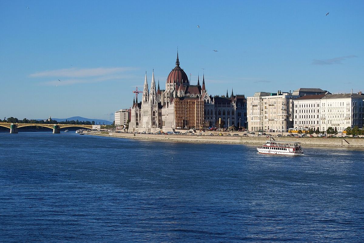 Parlamentul din Budapesta (Országház) și Dunărea, văzute de pe malul fluviului, cu o barcă turistică în prim-plan. Fotografie de arhivă.