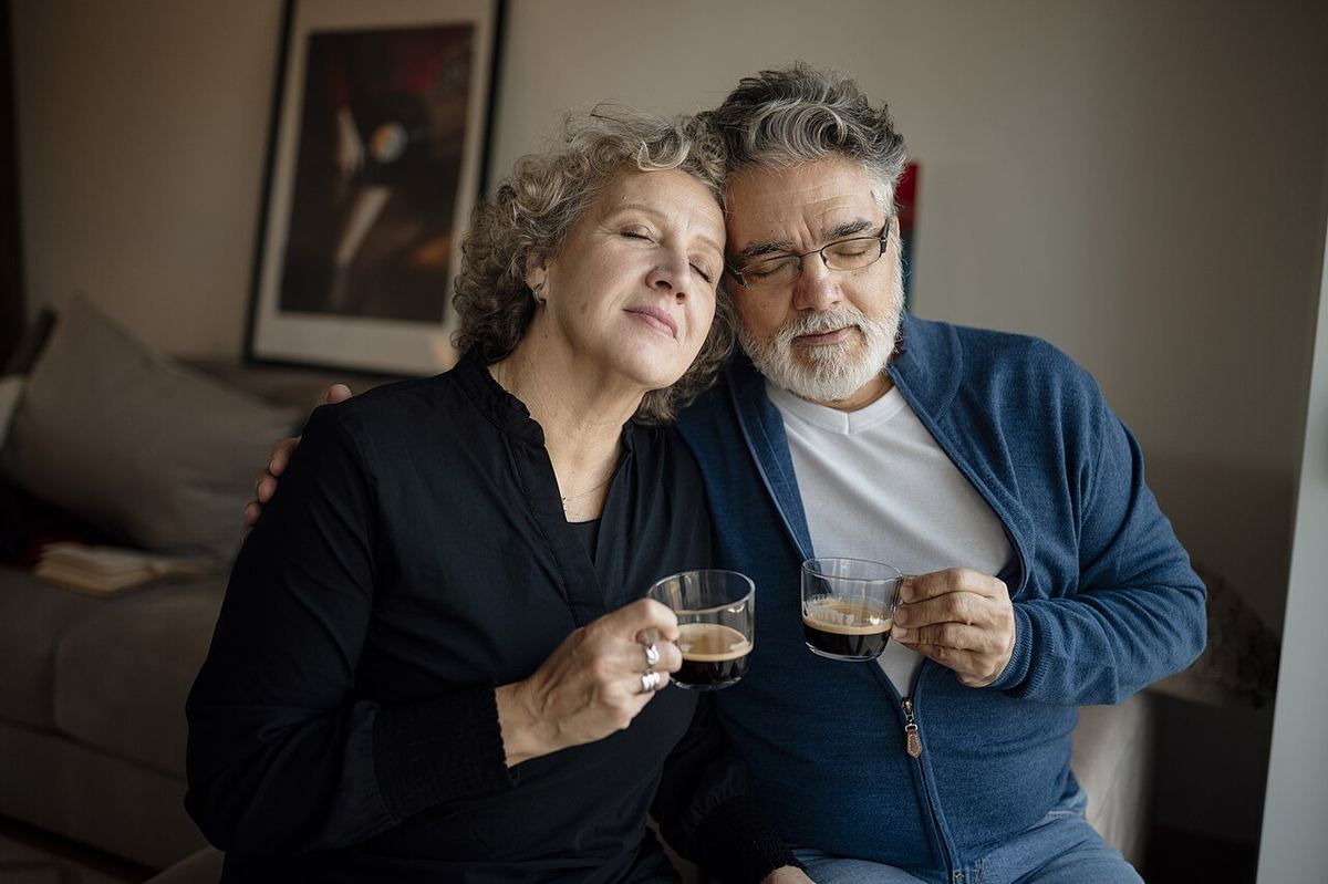 Un cuplu de vârstnici bea cafea împreună într-o cameră de zi confortabilă, în imagine de ilustrare.
