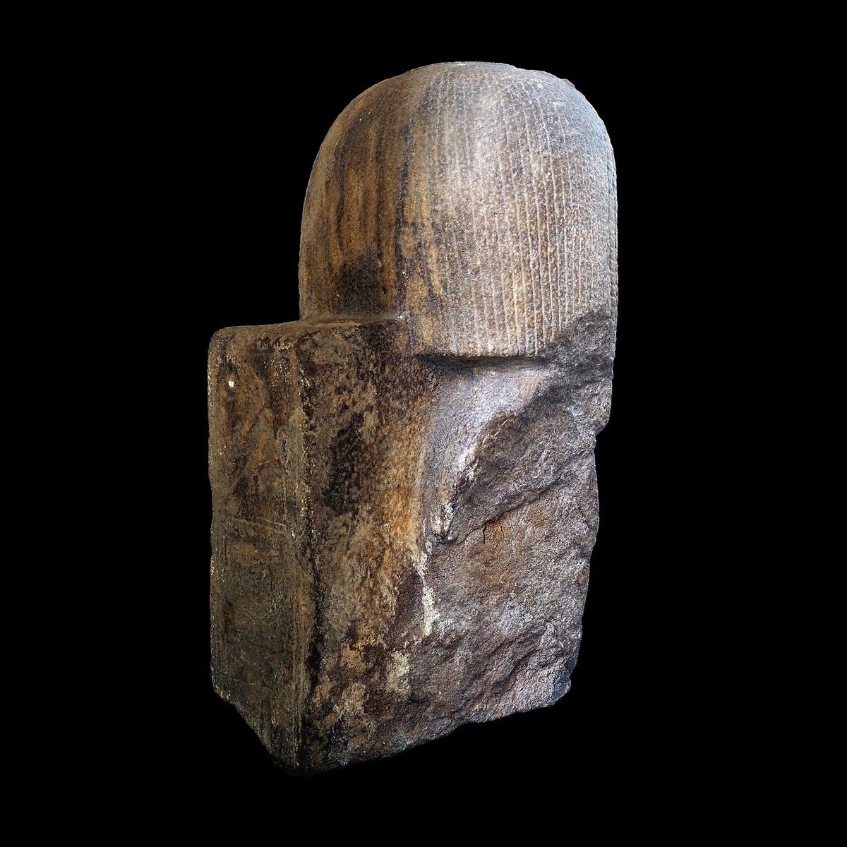 Statuie egipteană antică din piatră închisă la culoare, reprezentând un faraon, fotografiată pe un fundal întunecat.