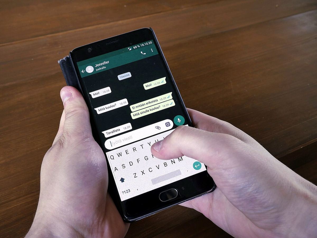 Mână care ține un telefon mobil cu o conversație WhatsApp deschisă și tastatura afișată pe ecran.