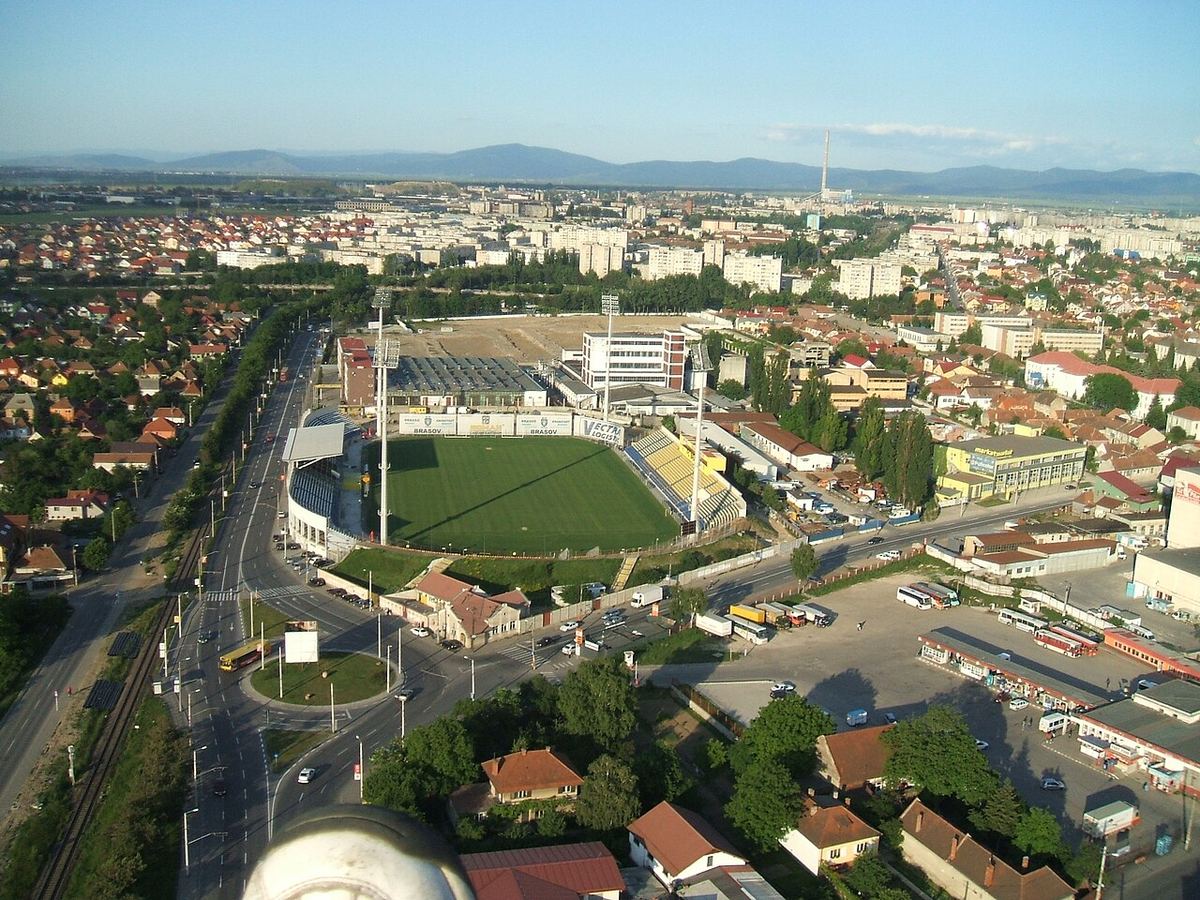 Vedere aeriană a Stadionului Tineretului din Brașov, cu stâlpii de nocturnă, tribunele și împrejurimile orașului.