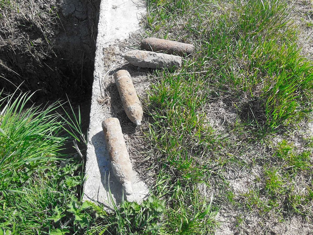 Patru obuze de artilerie neexplodate așezate pe marginea unui drum.