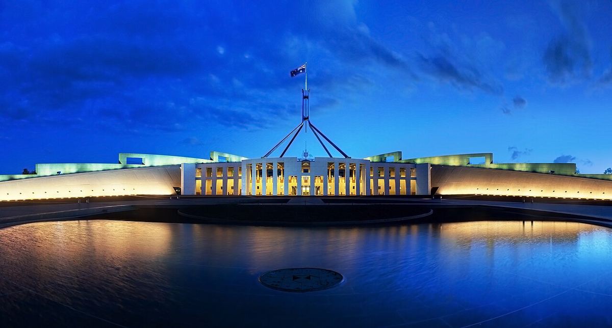 Clădirea Parlamentului Australiei din Canberra, iluminată seara, cu steagul australian pe catarg.