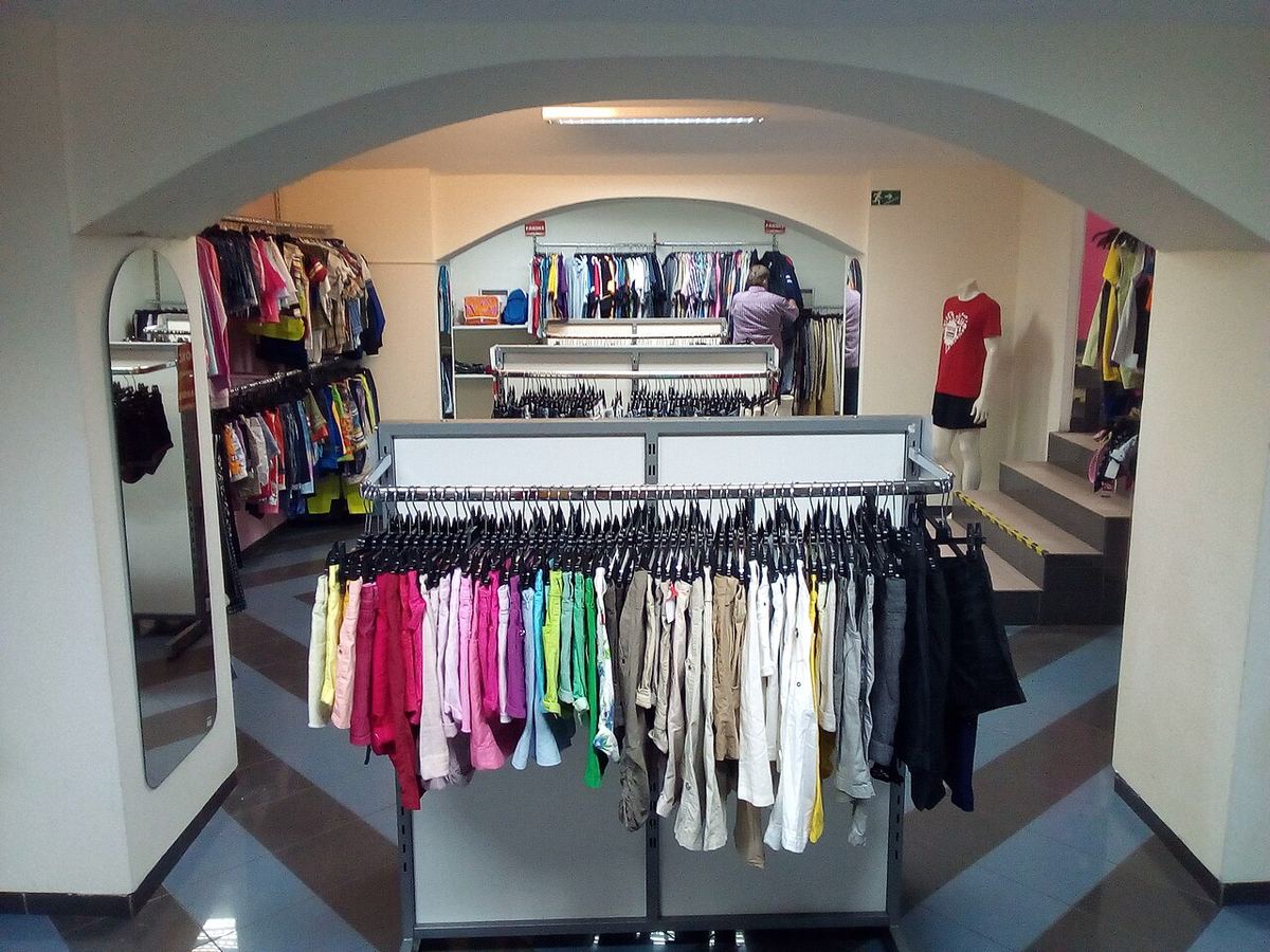 Interiorul unui magazin second-hand, cu rafturi pline de haine expuse pe umerașe.