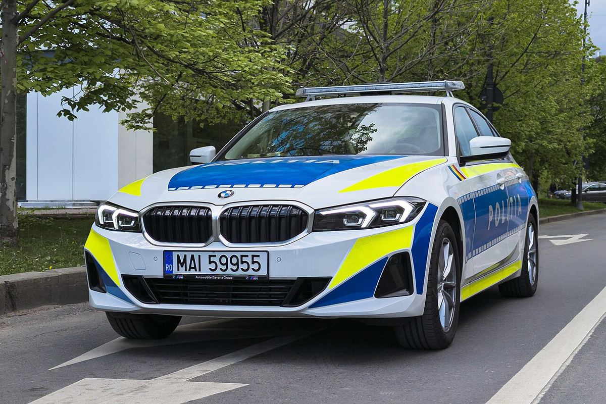 Mașină a Poliției Române BMW Seria 3 în livrea albă, albastră și galbenă, pe o stradă, ziua.