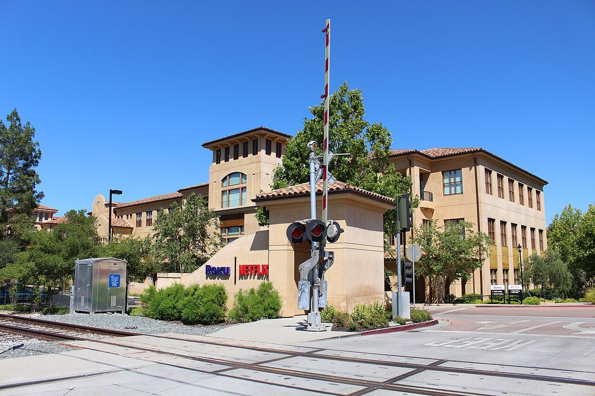 Sediul Netflix din Los Gatos, California, cu logo-ul companiei pe un panou lângă o trecere la nivel cu calea ferată.