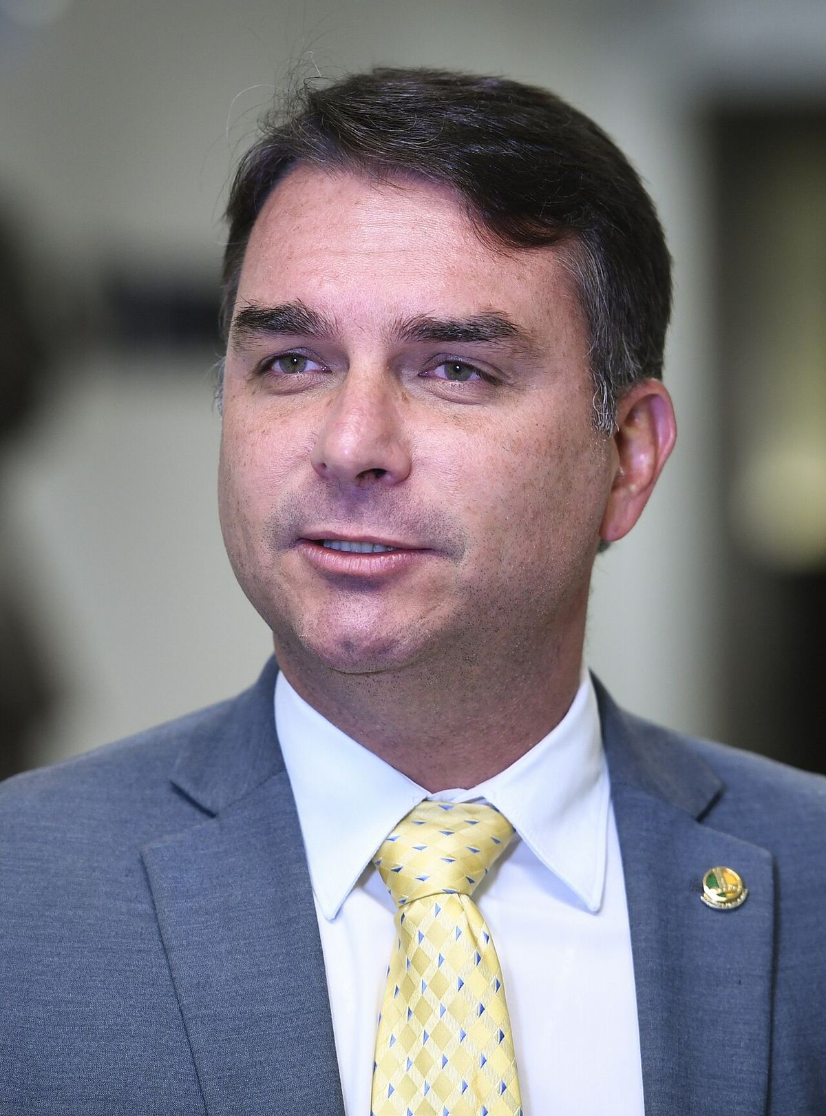 Senatorul Flávio Bolsonaro (PL-RJ) acordă un interviu, în costum gri, cămașă albă și cravată galbenă.