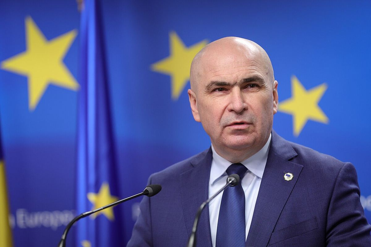 Ilie Bolojan vorbind la microfon, în fața steagurilor UE, în 2025