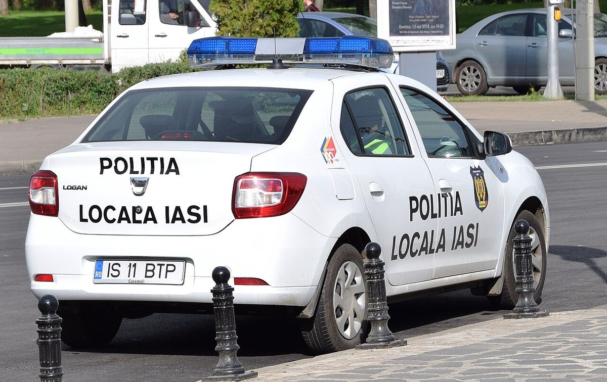 Autoturism alb al Poliției Locale Iași, cu girofar albastru, parcat pe o stradă din Iași, ziua.