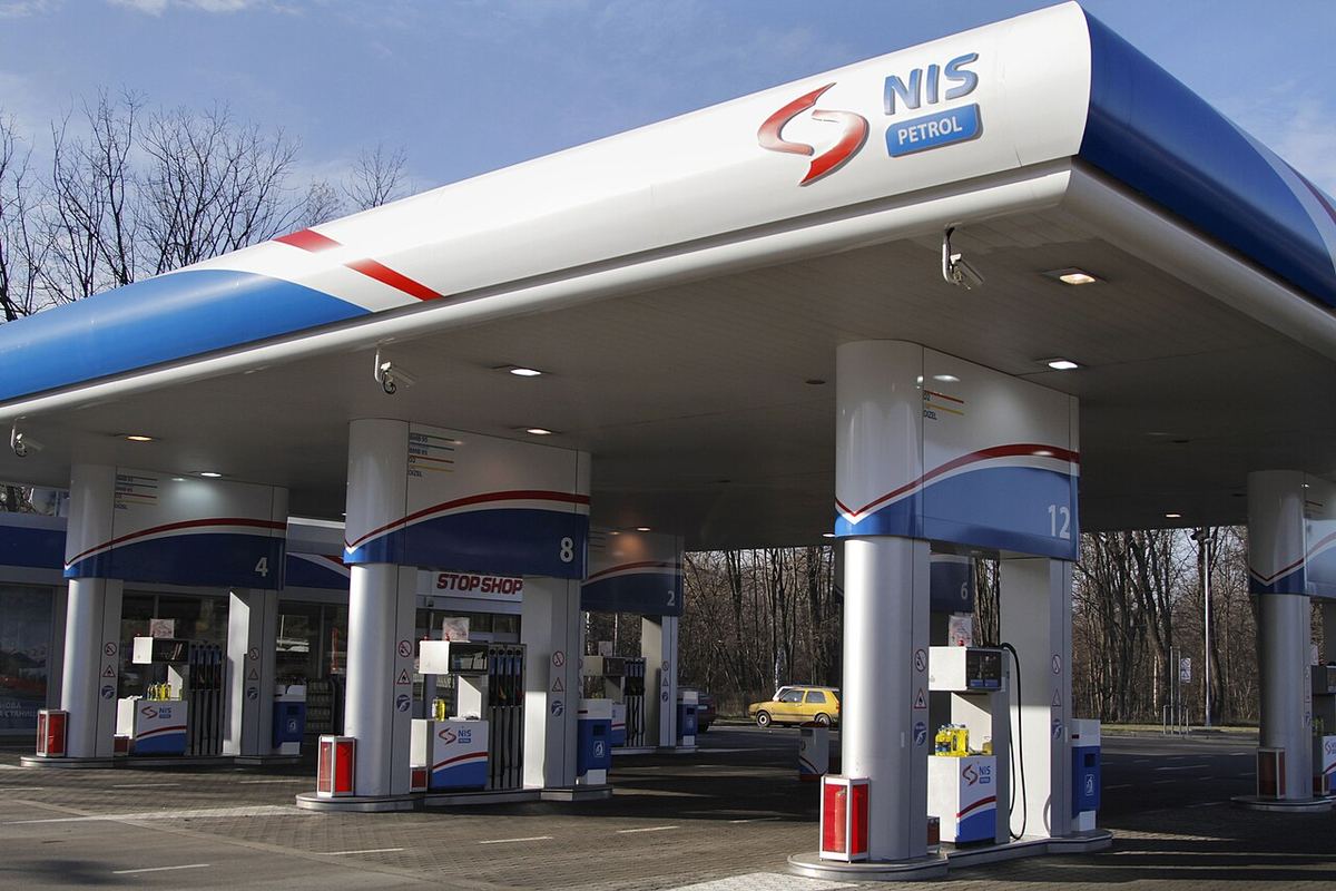 Benzinărie NIS Petrol cu logo-ul companiei și pompe de carburant, fotografiată ziua, în fața unui magazin.