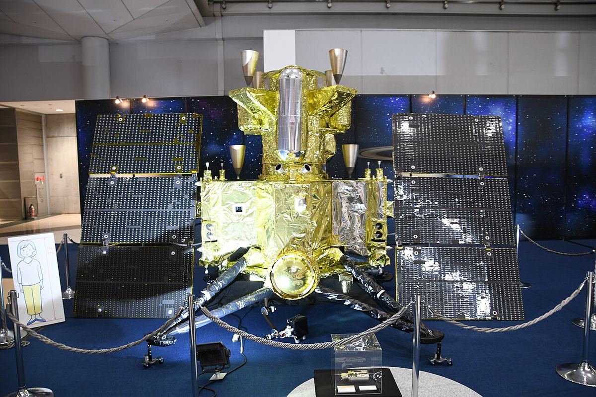 Macheta la scară 1:2 a sondei japoneze MMX, expusă la un salon aerospațial din Tokyo, cu panouri solare și corp aurit.