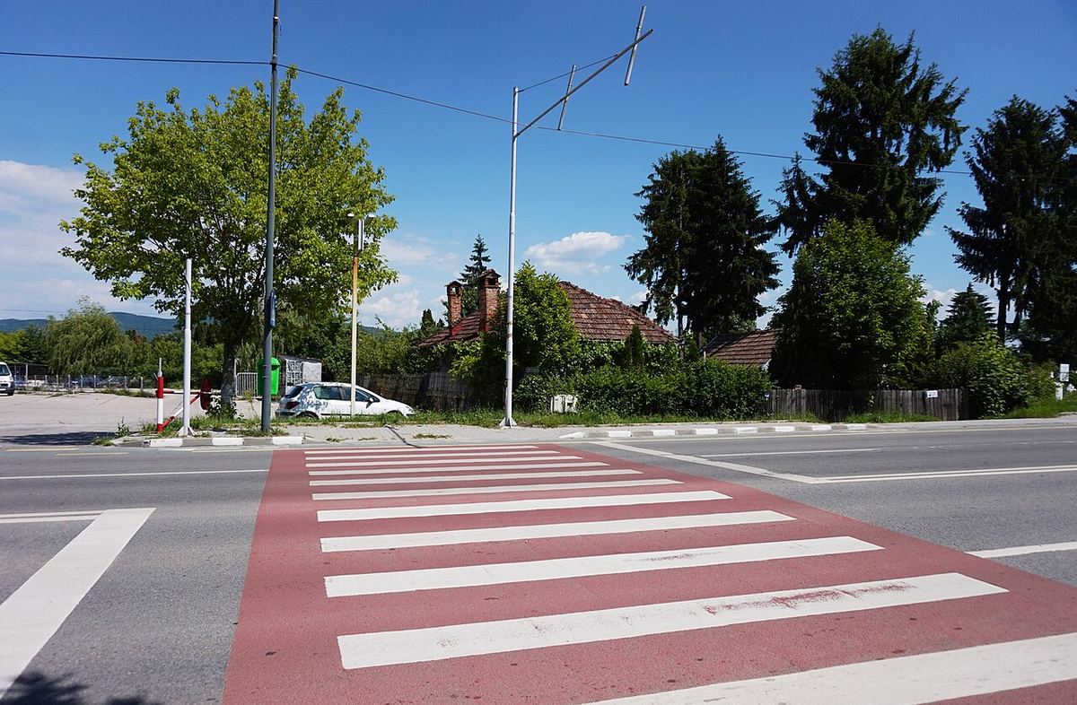 Trecere de pietoni marcată cu dungi albe pe asfaltul unei străzi urbane.