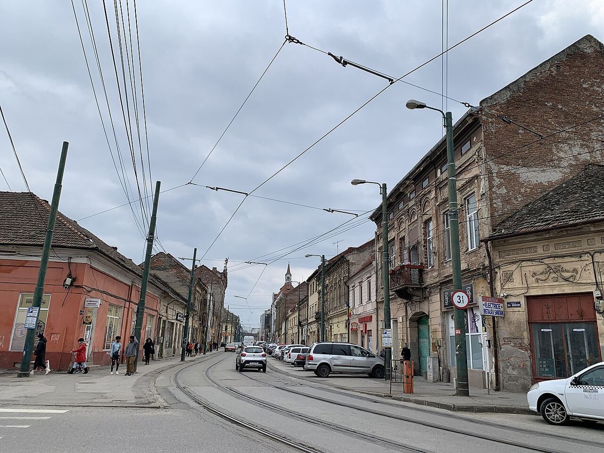 Imagine ilustrativă a unei străzi urbane cu clădiri și trotuare, de-a lungul unui bulevard din oraș.