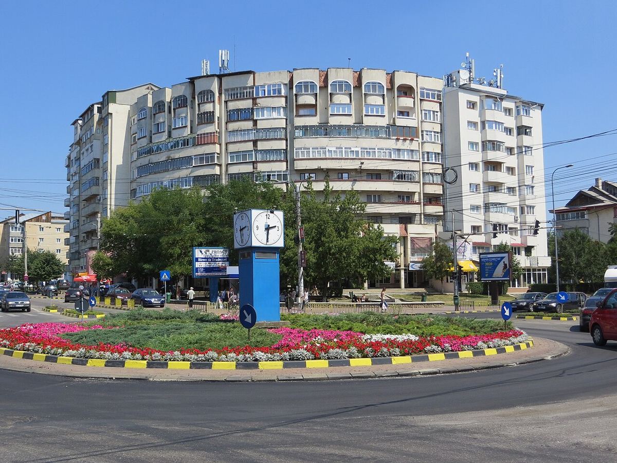 Sens giratoriu cu flori și bordură galben-negru în cartierul Burdujeni din Suceava, cu blocuri în fundal.