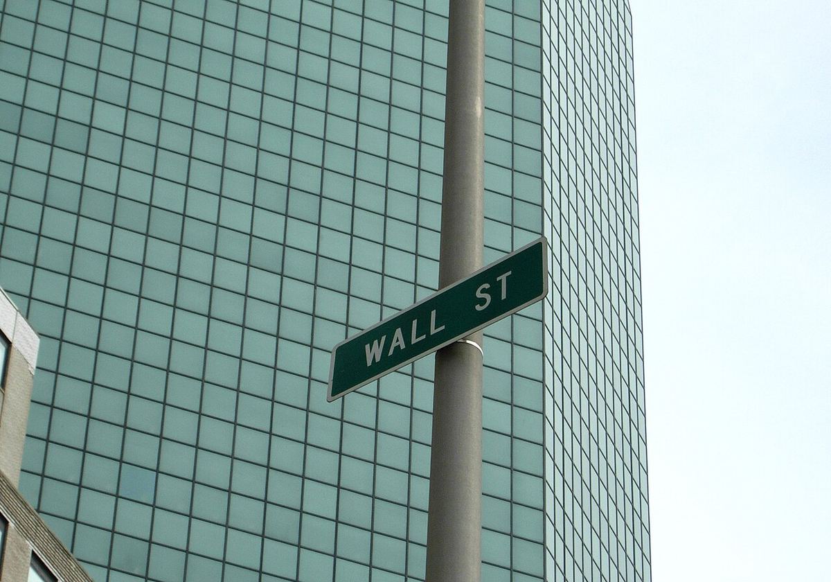 Plăcuța stradală Wall Street din New York, în fața unei clădiri înalte cu fațadă de sticlă.