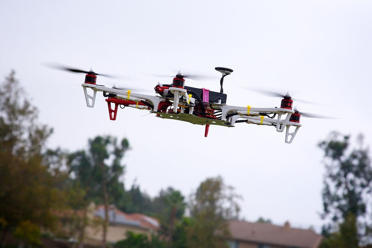 Dronă cu șase elice zburând deasupra unei zone cu copaci și case, fotografie de arhivă.
