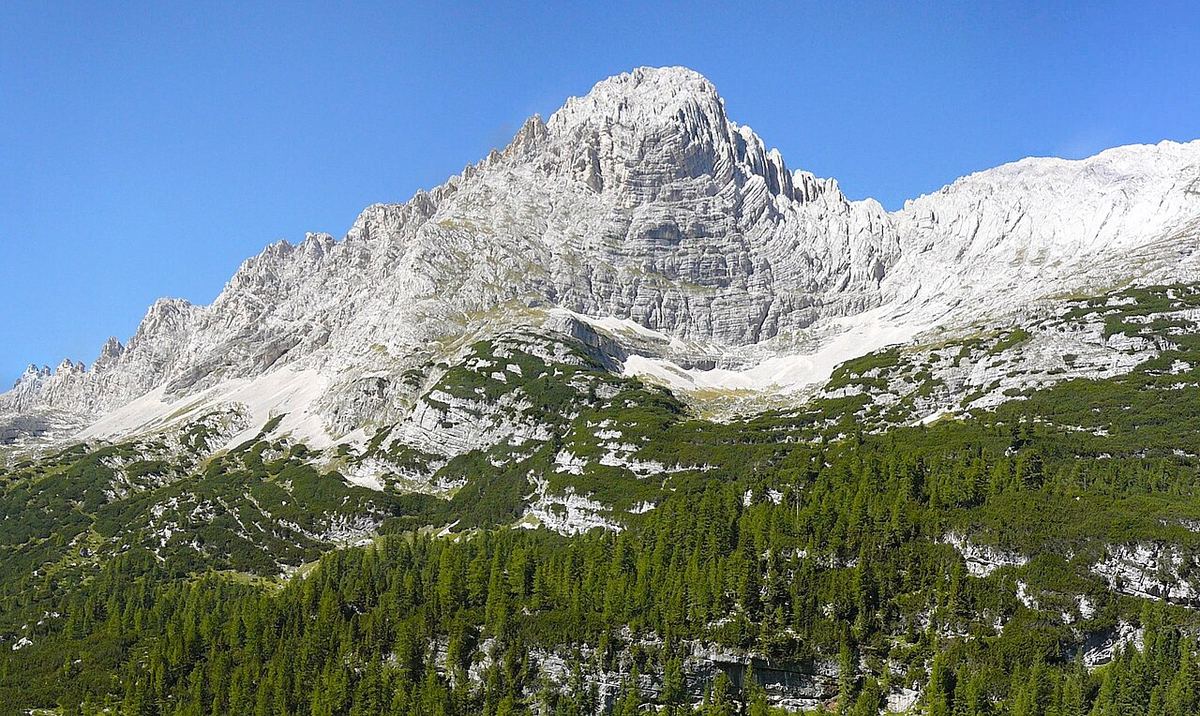 Peisaj montan cu vârf stâncos și versanți abrupți, imagine ilustrativă a unei zone alpine.