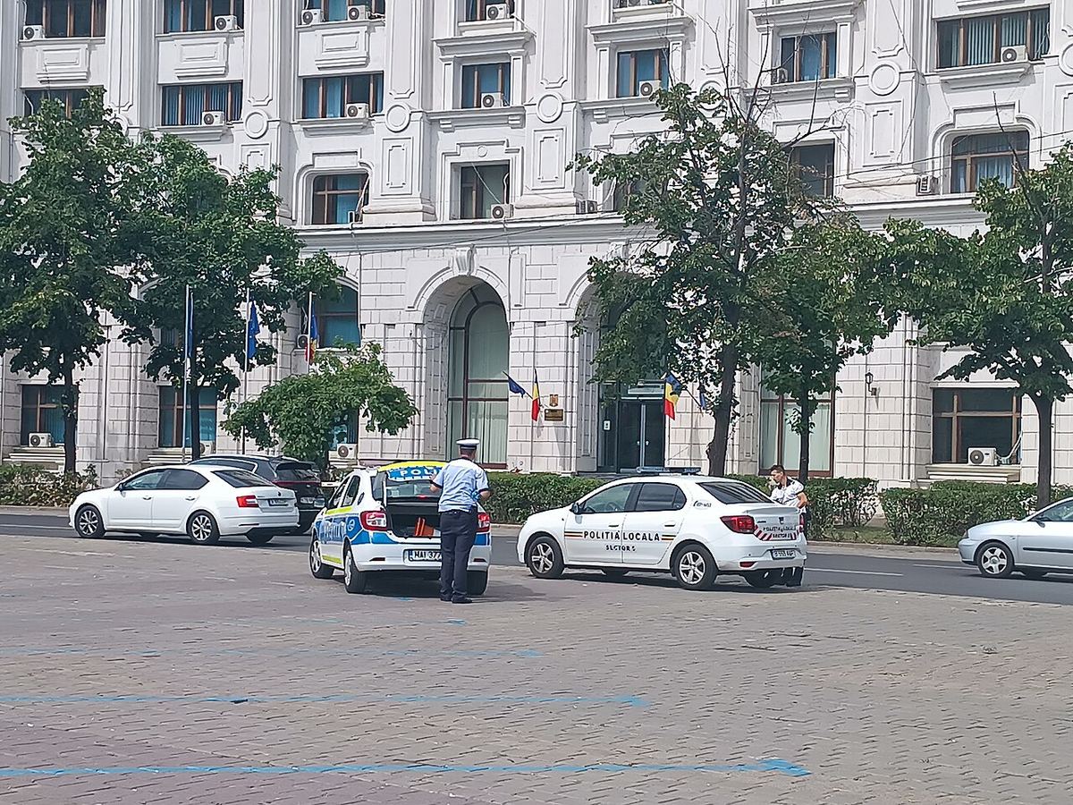 Mașini de poliție și un polițist în uniformă în fața unei clădiri administrative din București.
