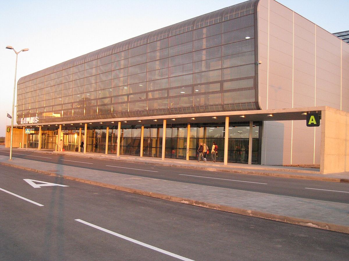 Terminalul A al aeroportului din Kaunas, Lituania, fotografiat la apus, cu câțiva pasageri în fața clădirii.
