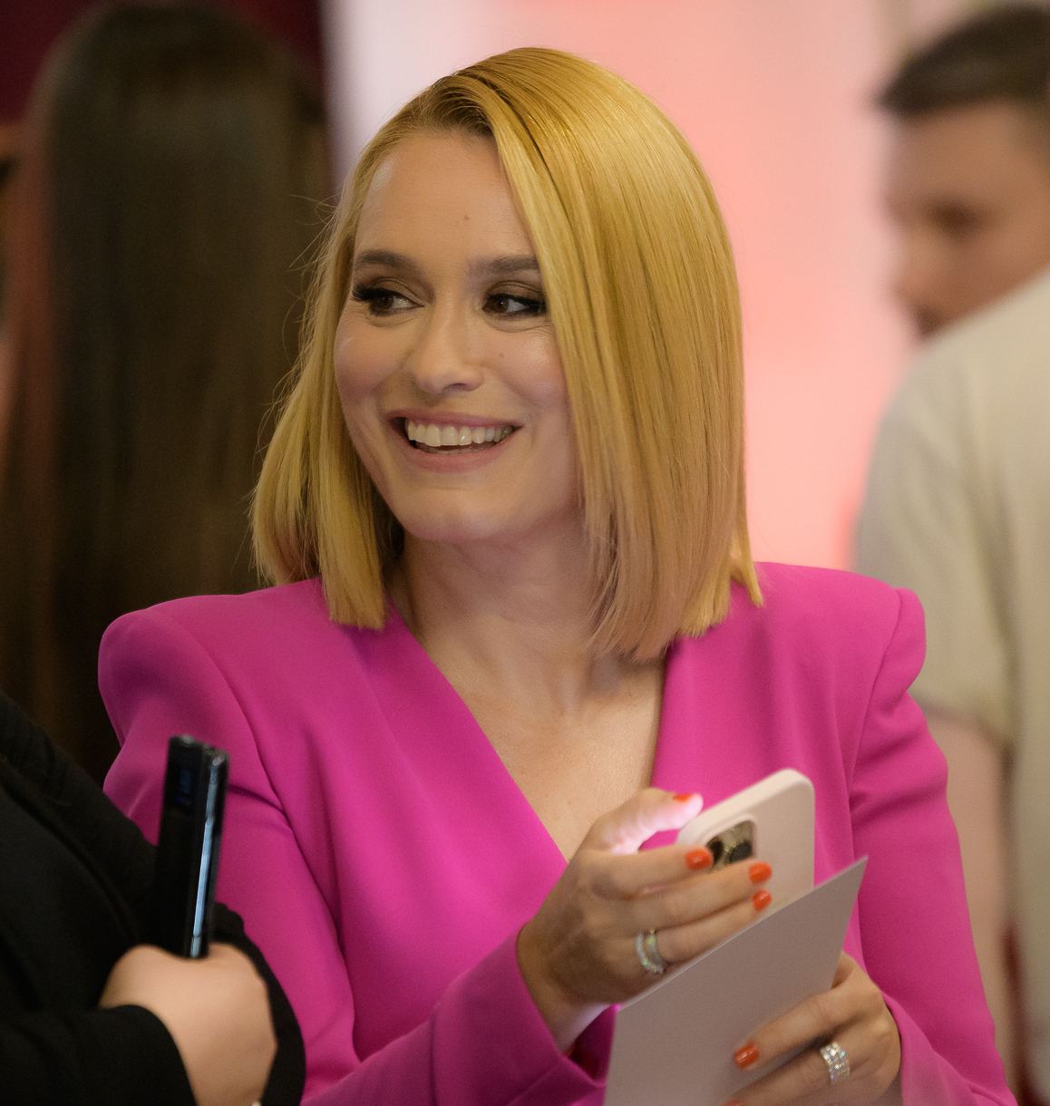 Andreea Esca zâmbind, îmbrăcată într-un sacou roz, ținând un telefon mobil la un eveniment (fotografie de arhivă).
