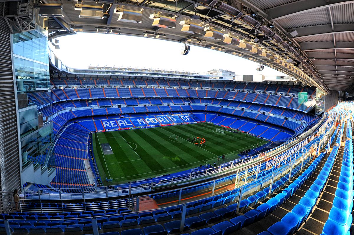 Stadionul Santiago Bernabéu din Madrid, cu tribunele goale și terenul de fotbal verde, fotografiat din tribuna superioară.