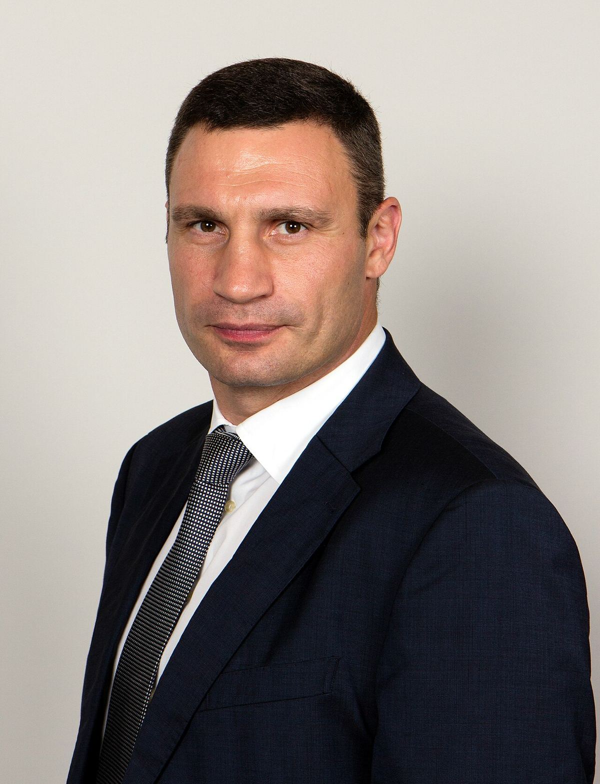 Fotografie de arhivă a primarului Kievului, Vitali Kliciko, în costum închis și cămașă albă, pe fundal gri.
