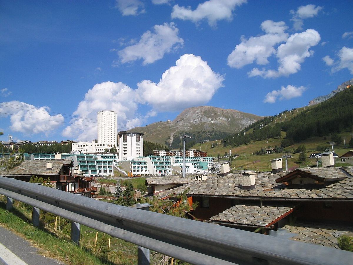 Vedere a localității Sestriere din Alpii Piemontului, cu clădiri înalte, acoperișuri de piatră și munți în fundal.
